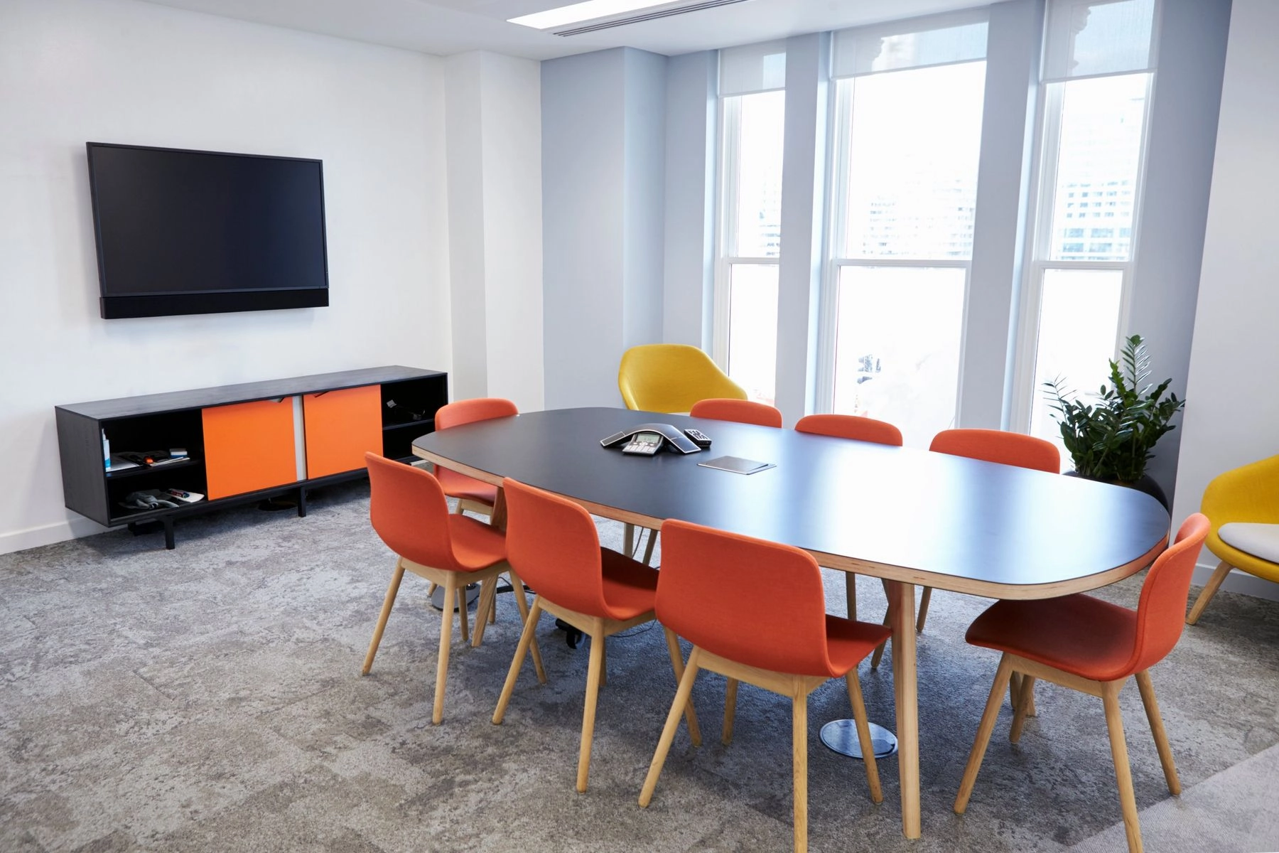 Meeting room with a wall-mounted display and soundbar, a conference table and orange chairs
