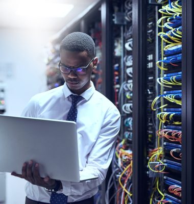 Cropped shot of a IT technician working on his laptop while standing inside of a server room.