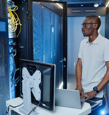 Side view portrait of black men setting up internet network and using laptop in server room lit by neon light