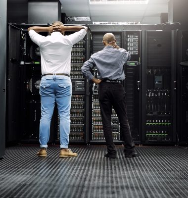 Rearview shot of two IT technicians having difficulty repairing a computer in a server room.